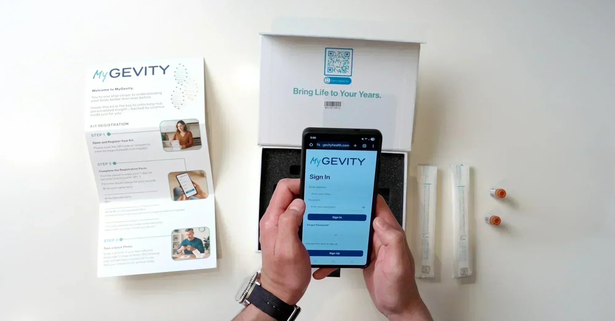 A person’s hands holding a smartphone displaying the MyGevity sign-in page over an open DNA testing kit, including instructional guides and collection swabs on a white surface.