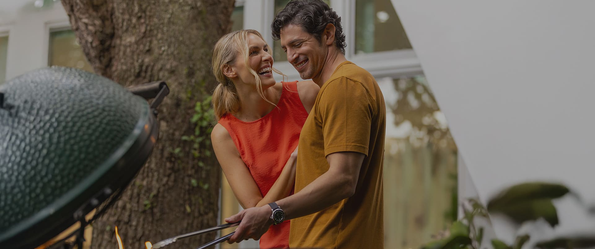 Man and woman grilling outdoors with a large green grill in the foreground.