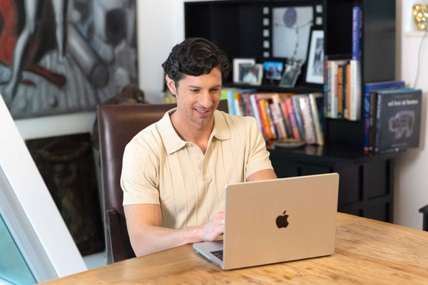 Man using a laptop at a desk with books and decor in the background